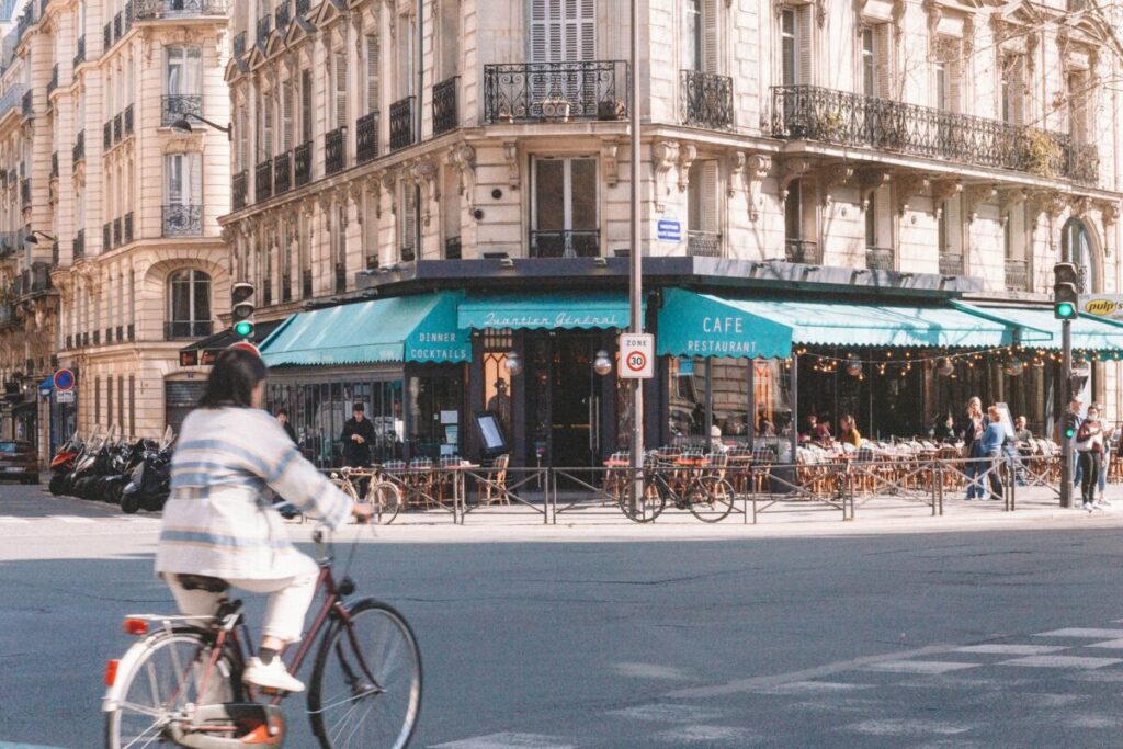 Woman cycling in Paris, France passing by a cafe restaurant