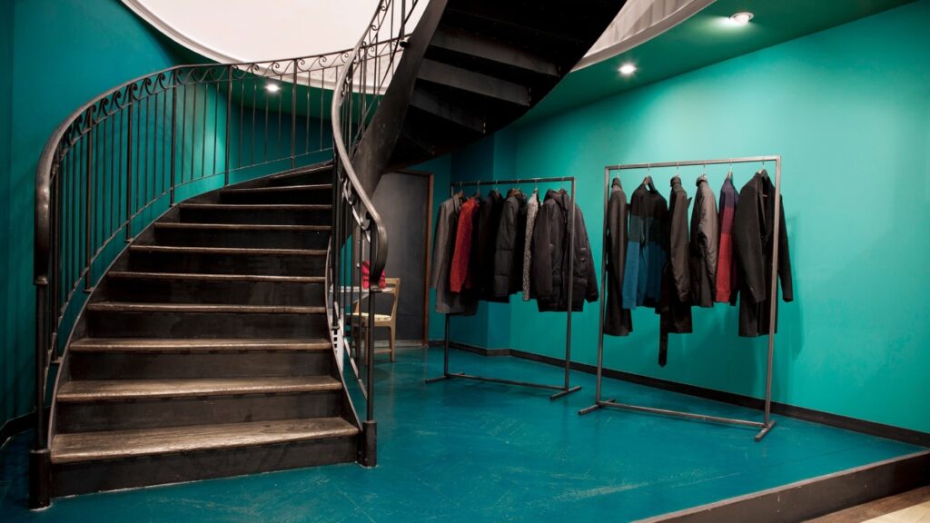 Interior view of Paul Smith Boulevard Raspail, highlighting a spiral staircase and a rack filled with clothes.
