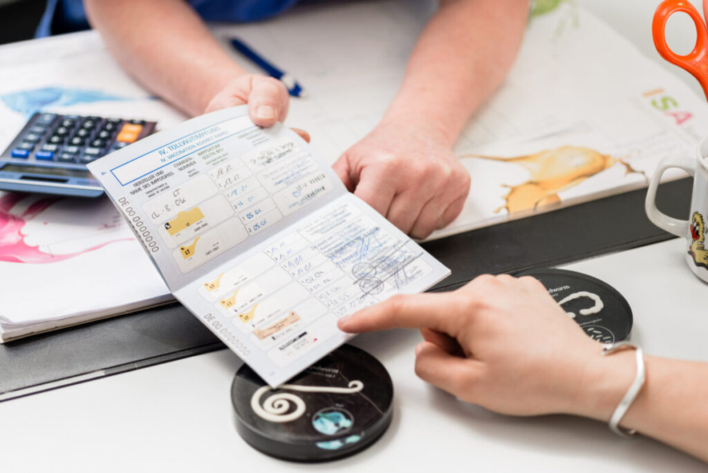 Close-up of two people at a desk showing a pet vaccination card, pointing at it.