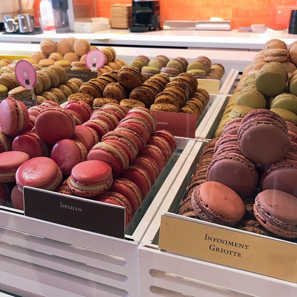 Display of colorful macarons in Pierre Hermé, including pink, brown, and green varieties. Each flavor is neatly stacked in trays, creating a vibrant, appetizing scene.