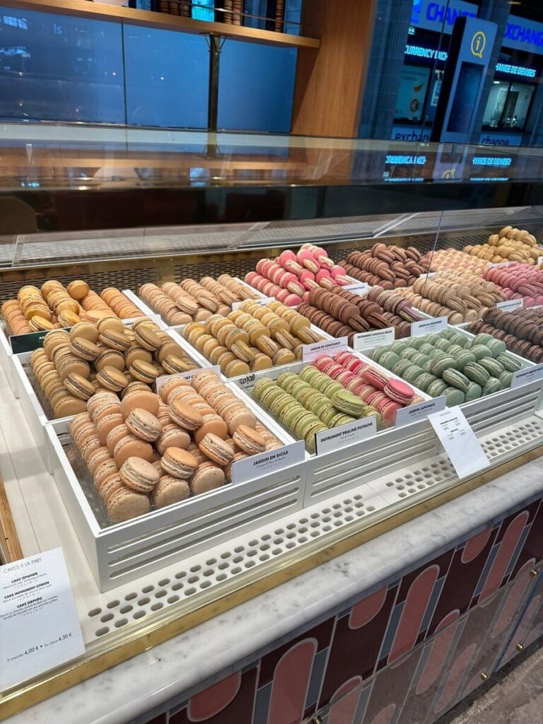 Pierre Hermé display case filled with assorted colorful macarons in neat rows. The inviting array includes hues of pink, green, brown, and yellow, creating a vibrant and tempting atmosphere.