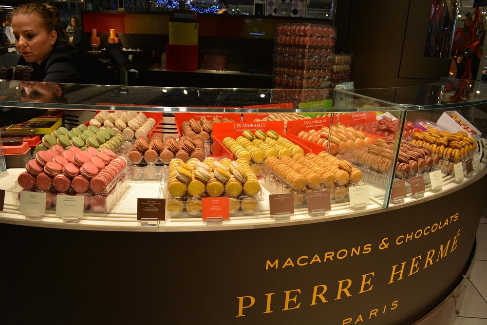 Pierre Hermé, Paris colorful display of assorted macarons in a Pierre Hermé shop. Rows of pink, green, brown, yellow, orange, and purple macarons are neatly arranged.