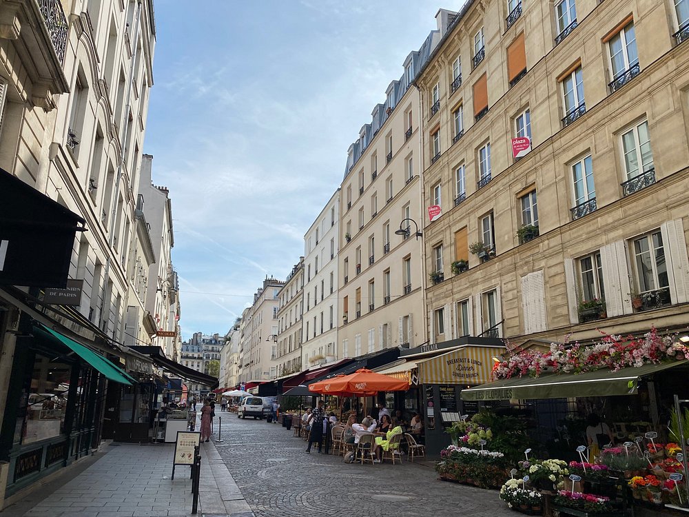 Rue Cler Market in Paris features a narrow street adorned with shops and colorful flowers in the middle.