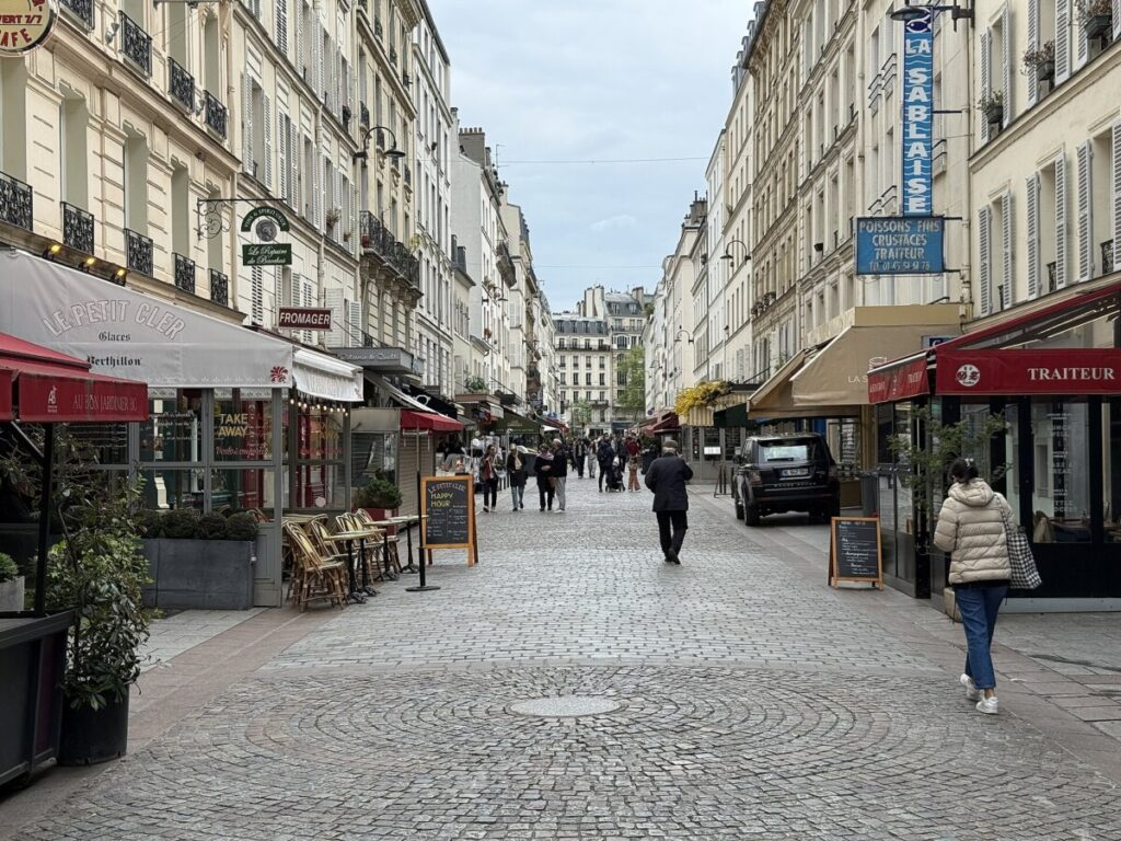 Charming Parisian street lined with cozy shops, featuring quaint architecture and vibrant storefronts under a clear blue sky.