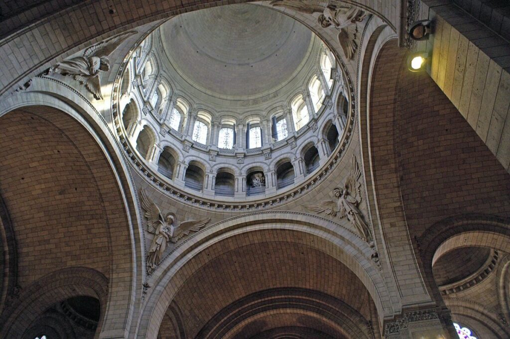 Interior view of a grand dome in Sacré-Cœur Basilica, Paris, showcasing intricate carvings and angelic statues with soft, atmospheric lighting.