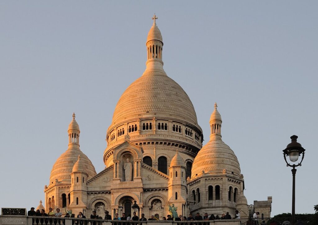 The Basilica of Sacré-Cœur in Paris, featuring its iconic white dome, set against a clear blue sky.