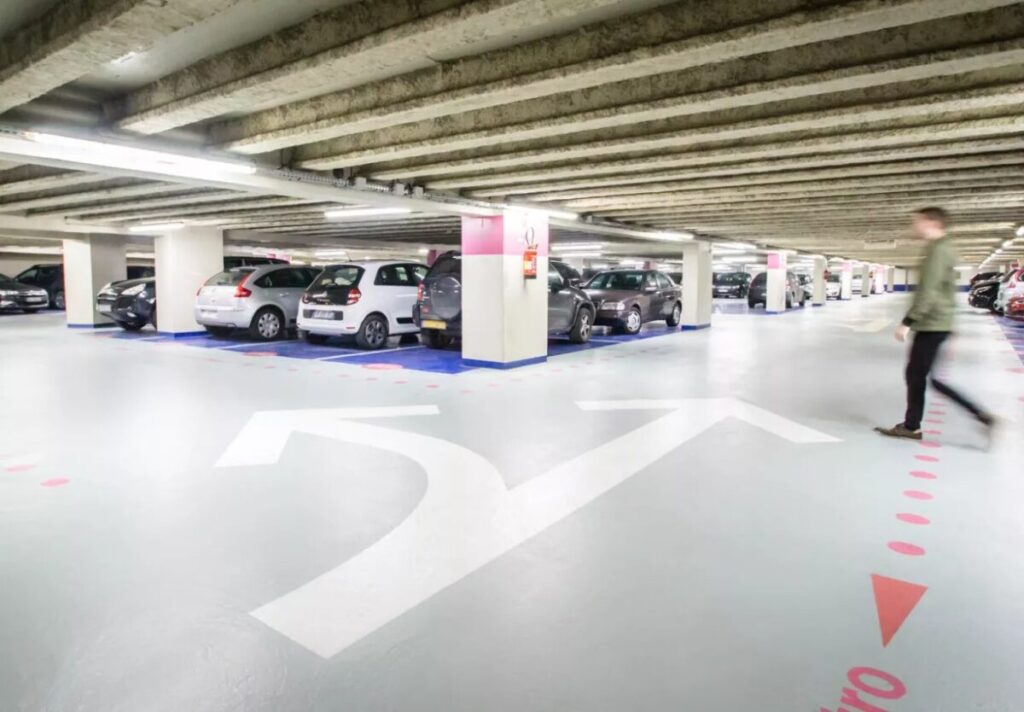 Man walks through the Saeme Parking space in Porte Dorléans , surrounded by parked cars in a spacious garage.