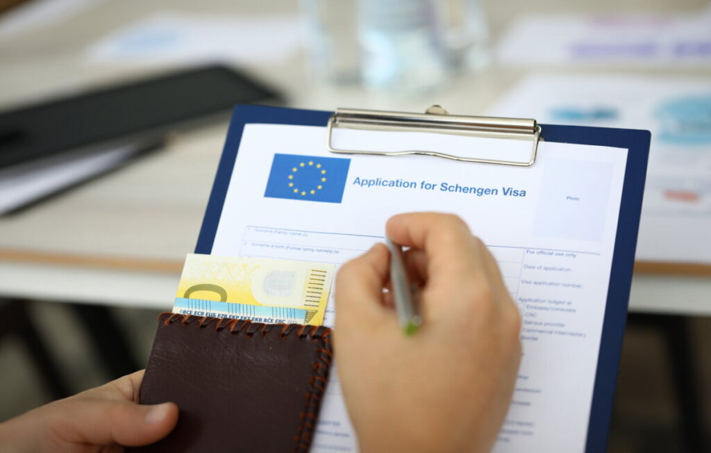 Hand holds a paper folder and passport with money, answering questions for a Schengen visa application.