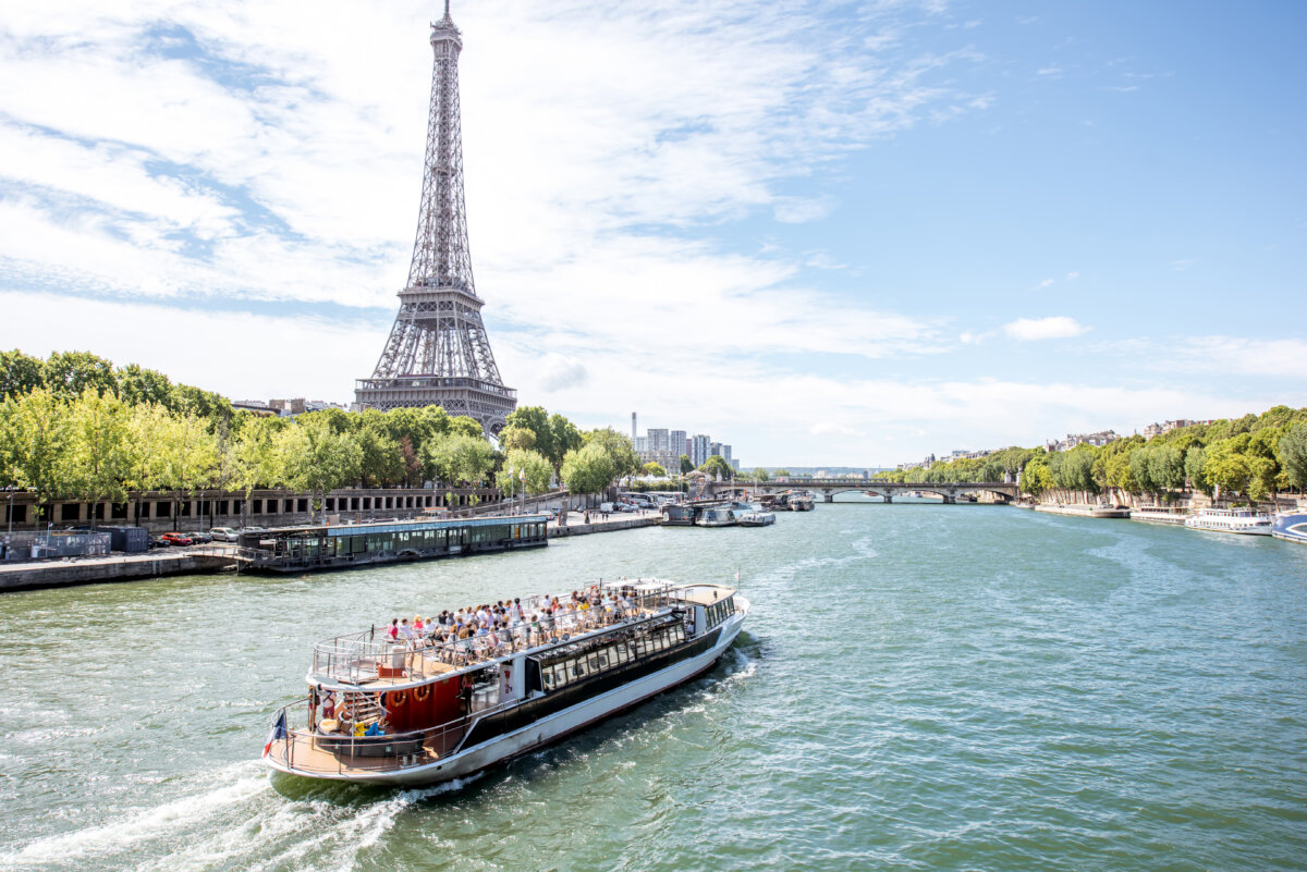 Scenic view of the Eiffel Tower and Seine River, featuring a tourist boat cruising through the heart of Paris.