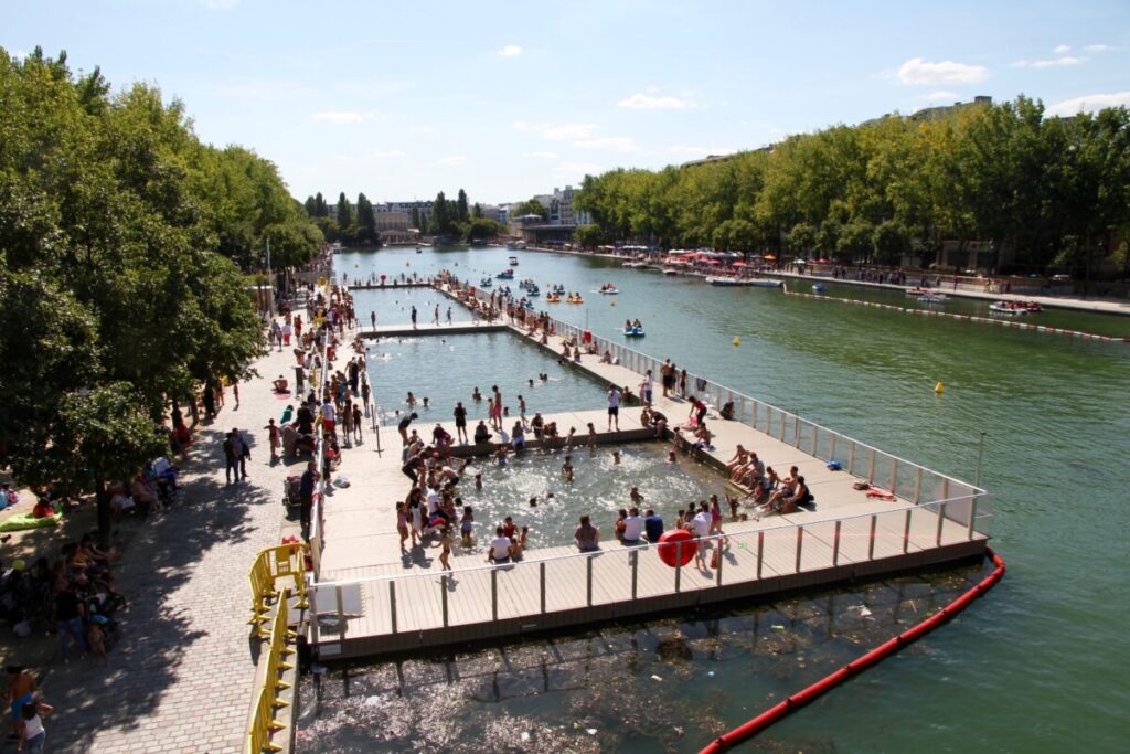 Scenic view of Bassin de la Villette in Paris, featuring people swimming in the Seine River on a sunny day.