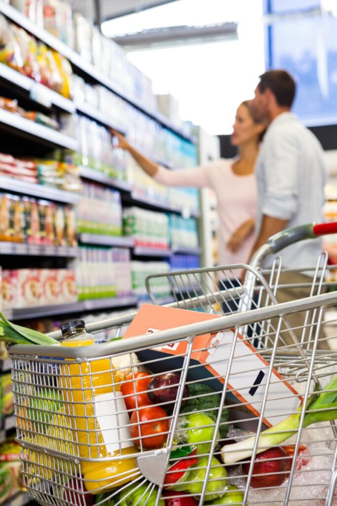 Shopping cart filled with various grocery items, including fruits, vegetables, and packaged goods.