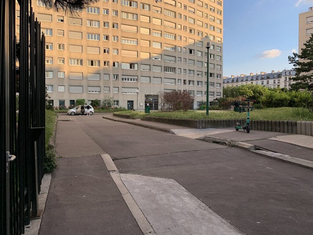 Street view of Square Nouveau Belleville in Paris, featuring a gate and a building in the background.