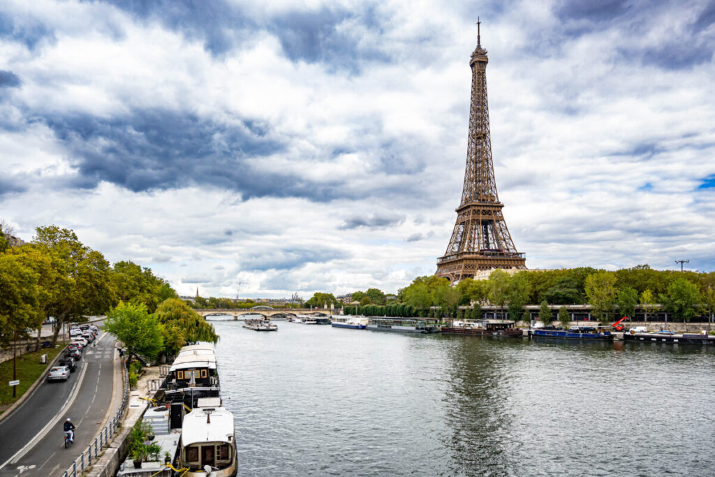 Eiffel Tower in Paris under a clear blue sky, bathed in sunlight, surrounded by green trees and vibrant flowers.
