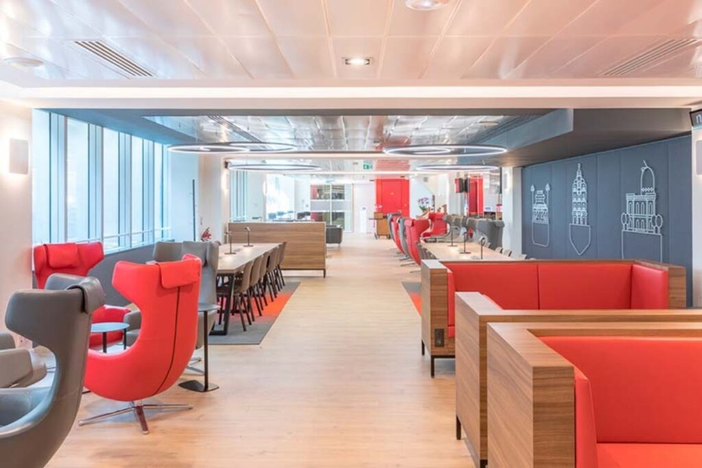 Interior of a TGV INOUI lounge with vibrant red chairs and tables set for guests.