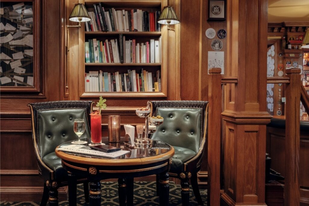 Interior of Bar Hemingway in Paris, showcasing a library with two chairs and a table for reading or conversation.