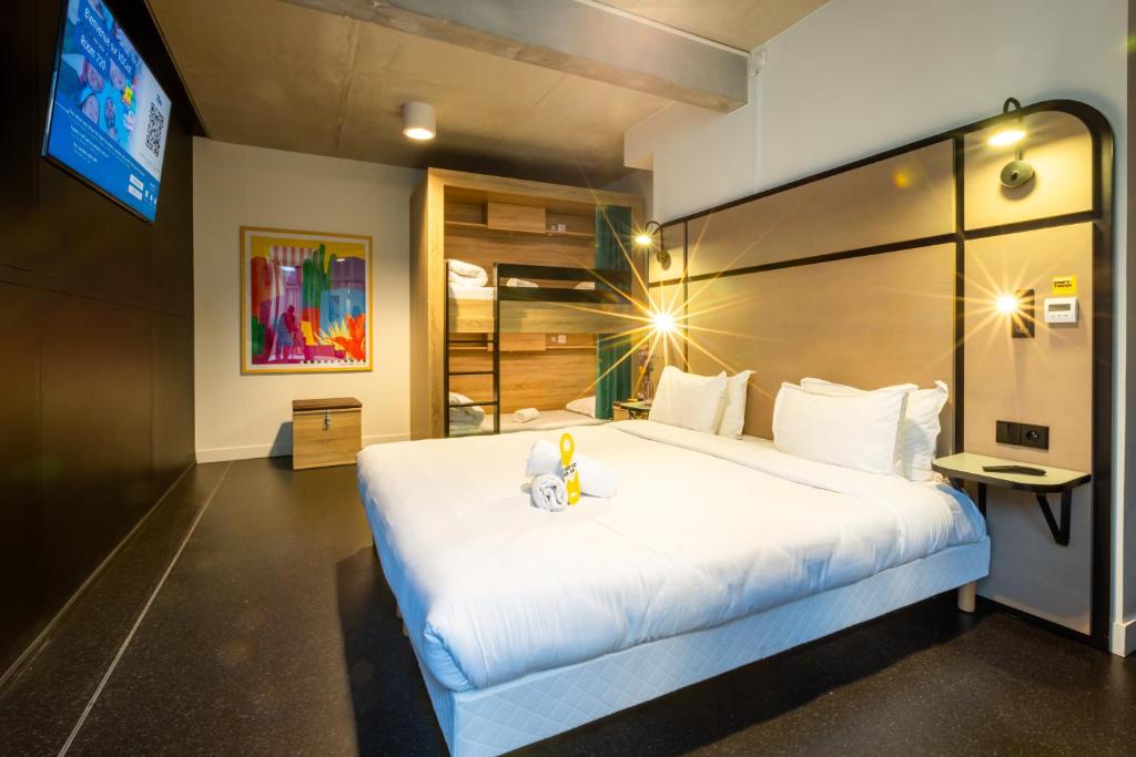Modern, cozy The People - Paris Marais hotel room with a neatly made bed, bright hanging lights, a wall-mounted TV, abstract artwork, and an open wardrobe with bunk beds.