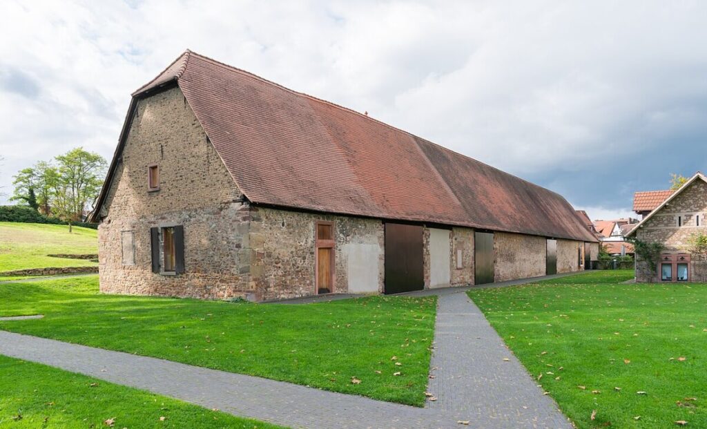 Tithe Barn in France featuring a prominent red roof, set against a lush grassy field.