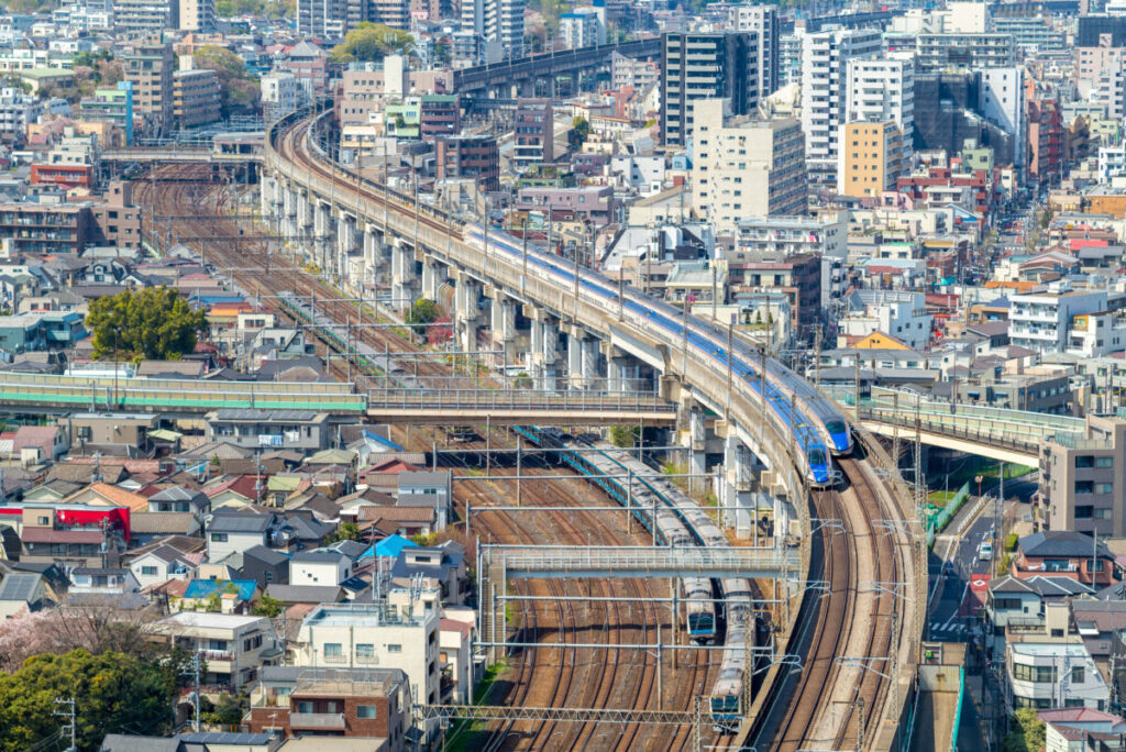 Aerial view of a bustling urban area with Tokyo, Japan blue train on elevated tracks curving through the city. Dense buildings surround the railway, showcasing city life.