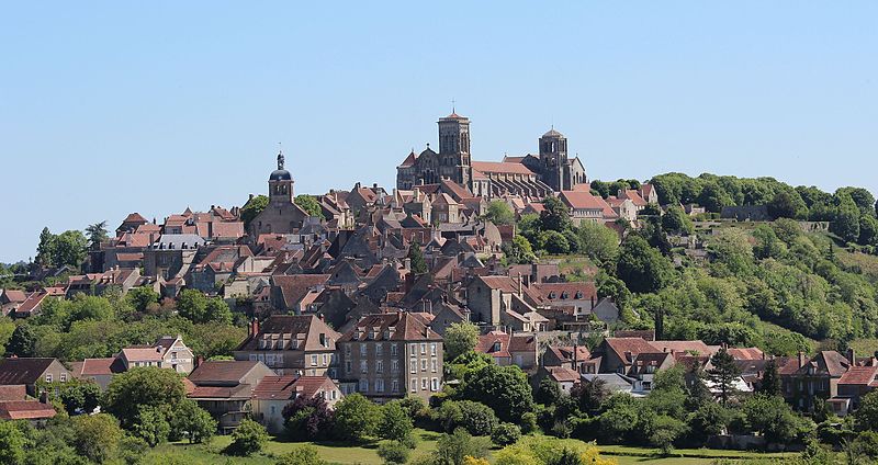 A view of Vézelay, a historic village in Burgundy, France, showing its medieval architecture and the famous Basilica of Saint Mary Magdalene, nestled on a hill surrounded by green countryside.