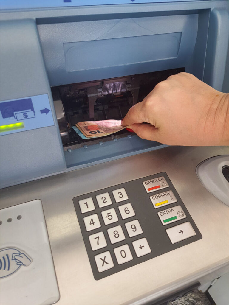 Woman's hand withdrawing cash from an ATM, with money being pulled from the machine.